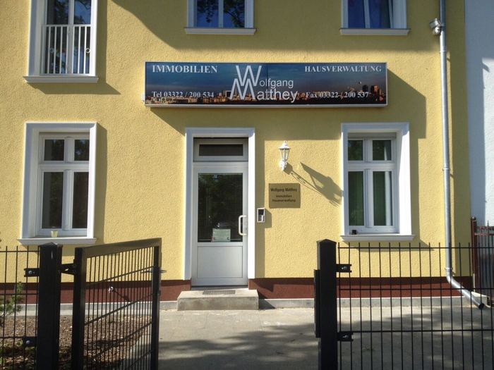 Eingang des Büros mit Firmenschild an der gelben Fassade
